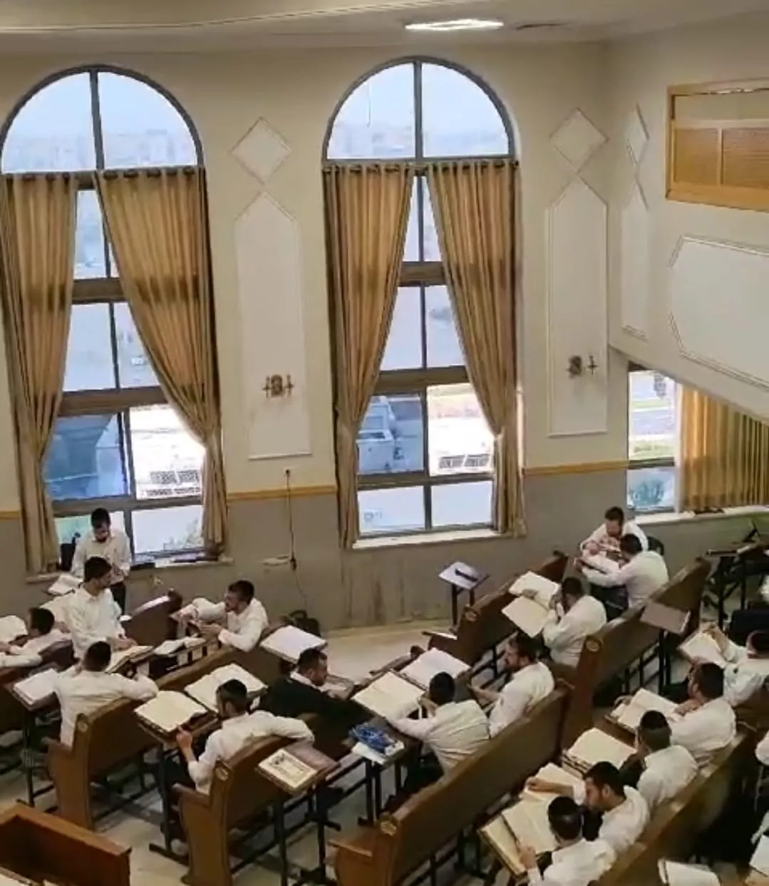 אולם בית המדרש: שורות שולחנות לימוד וספרים פתוחים, ומעליהם שני חלונות מקושתים